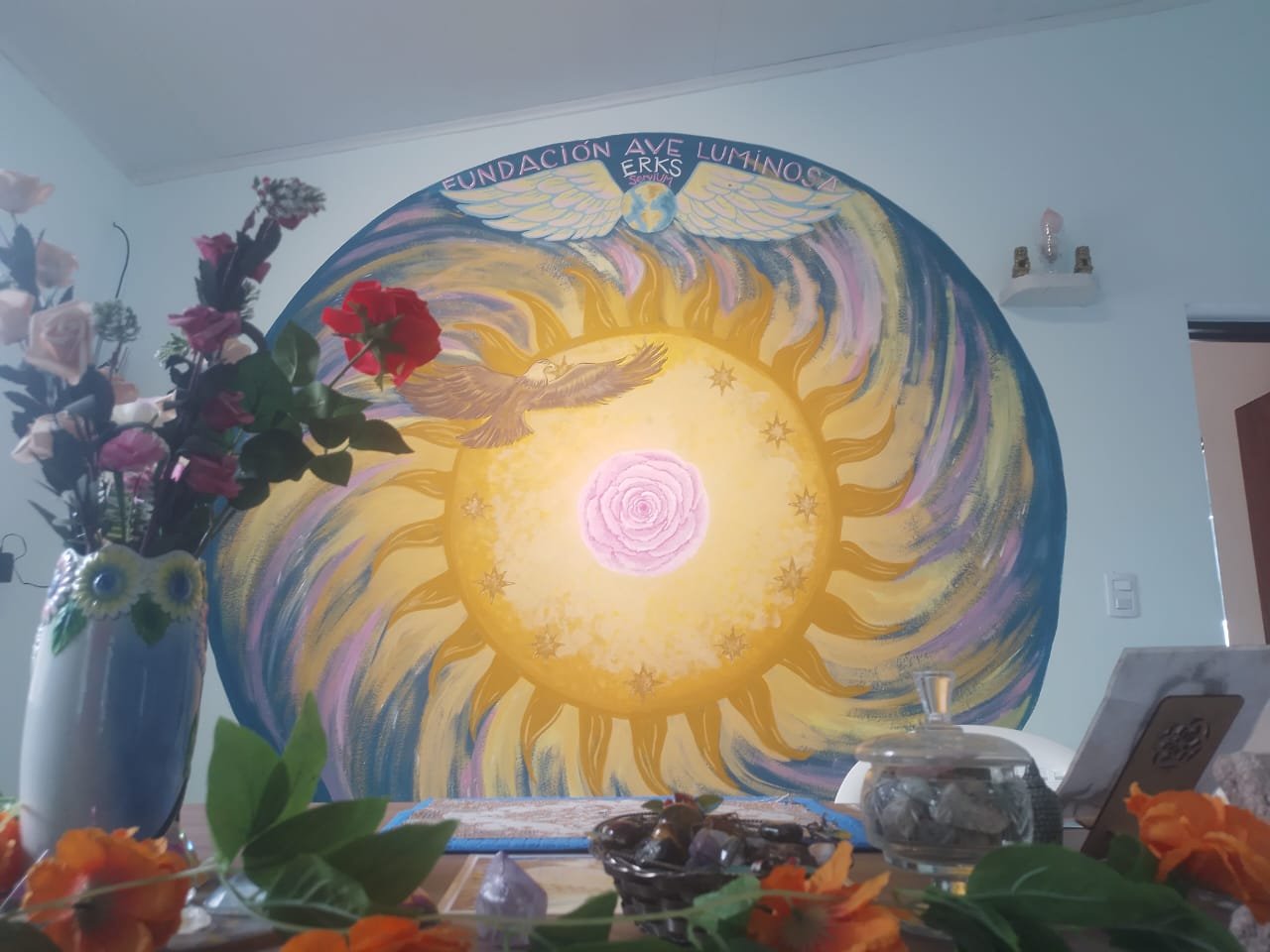 Altar con flores y cristales frente al mural de la Fundación Ave Luminosa